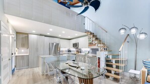 A modern kitchen with a glass dining table, stainless steel appliances, and a staircase with a railing. - Coquina Beach 3G- Gorgeous 2bd, plus loft, Sanibel beach condo! (Sanibel)