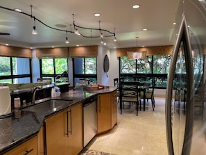 A modern kitchen with a central island, a dining area with chairs, and large windows with a view of greenery.