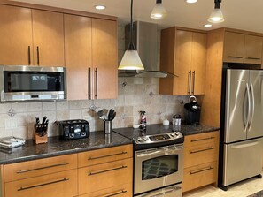 A modern kitchen with wooden cabinets, stainless steel appliances, and a granite countertop.