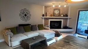 A modern living room with a sofa, coffee table, and dining table. There is a fireplace with a mantel and a hanging light fixture. - Negotiable! Hot tub, new kitchen and master bath.  (Frisco)