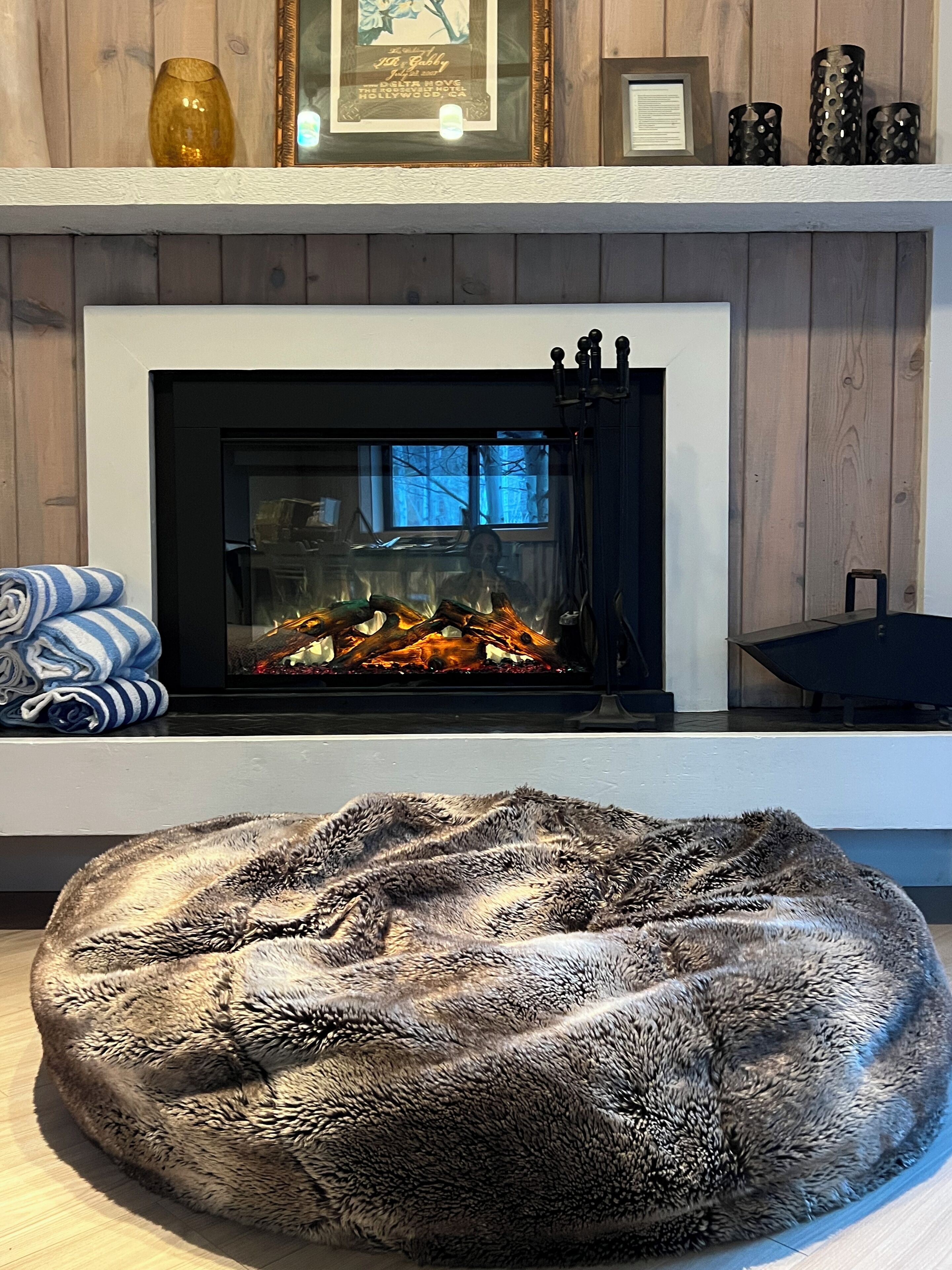 A fireplace with a visible fire, a plush fur rug, and a framed picture on the mantel.