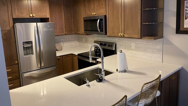 A modern kitchen with wooden cabinets, stainless steel appliances, a double sink, and a bar stool. - Negotiable! Hot tub, new kitchen and master bath.  (Frisco)