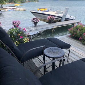 Eine Holzterrasse mit Sitzgelegenheiten im Freien, ein Boot schläft in der Nähe und der Blick auf einen ruhigen See.