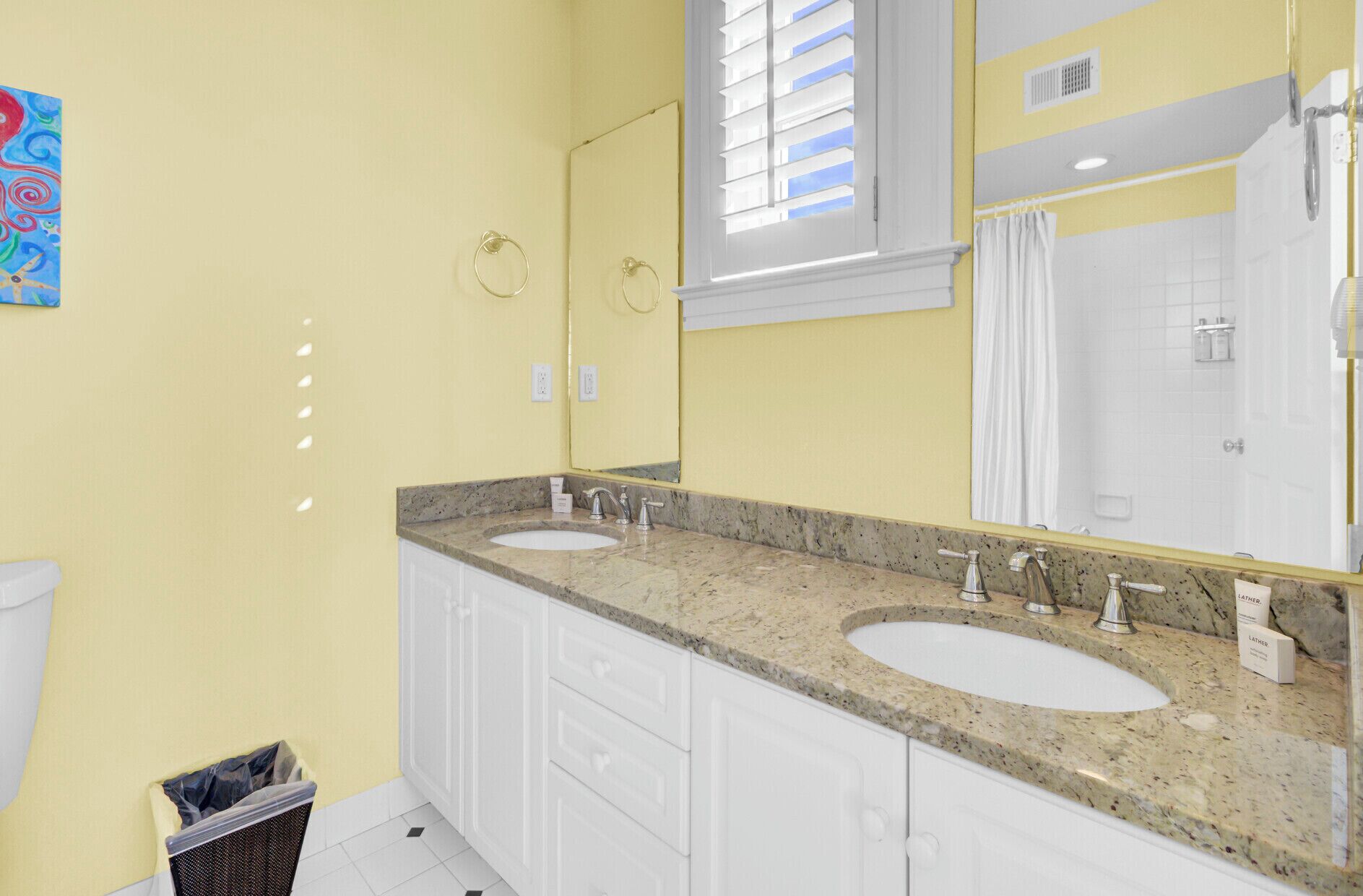 A bathroom with two sinks, a large mirror, and a window with blinds.