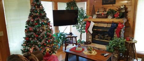 A cozy living room with a large Christmas tree, a fireplace, and a television.
