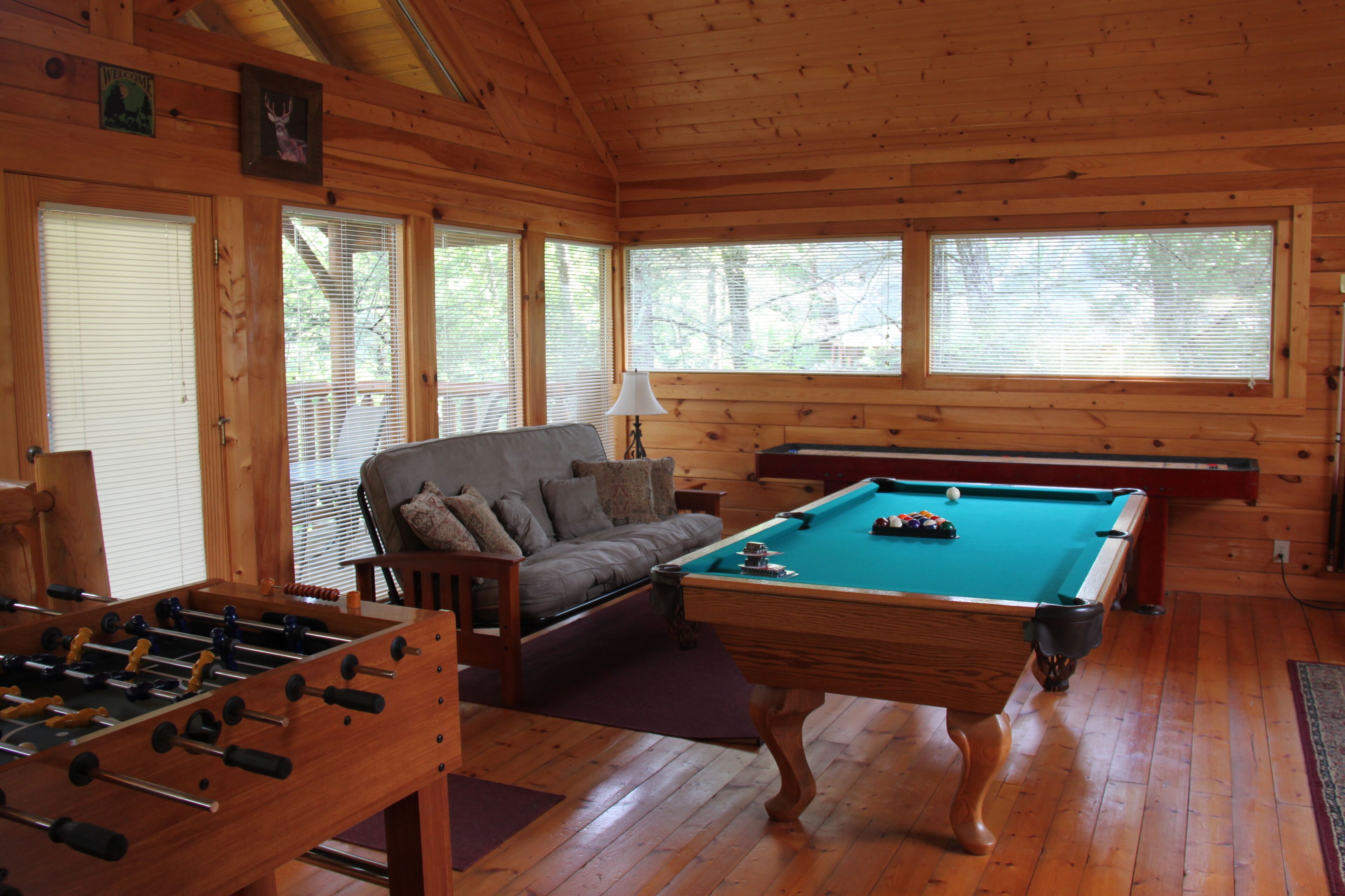 A wooden-floored room with a pool table, sofa, and foosball table.