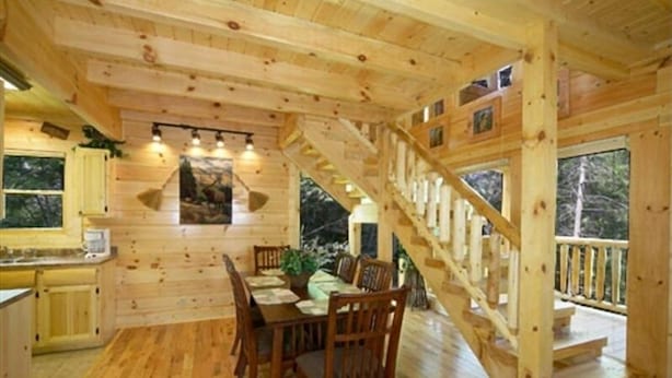 Een houten cabin met een eethoek, keuken en een trap naar een terras.