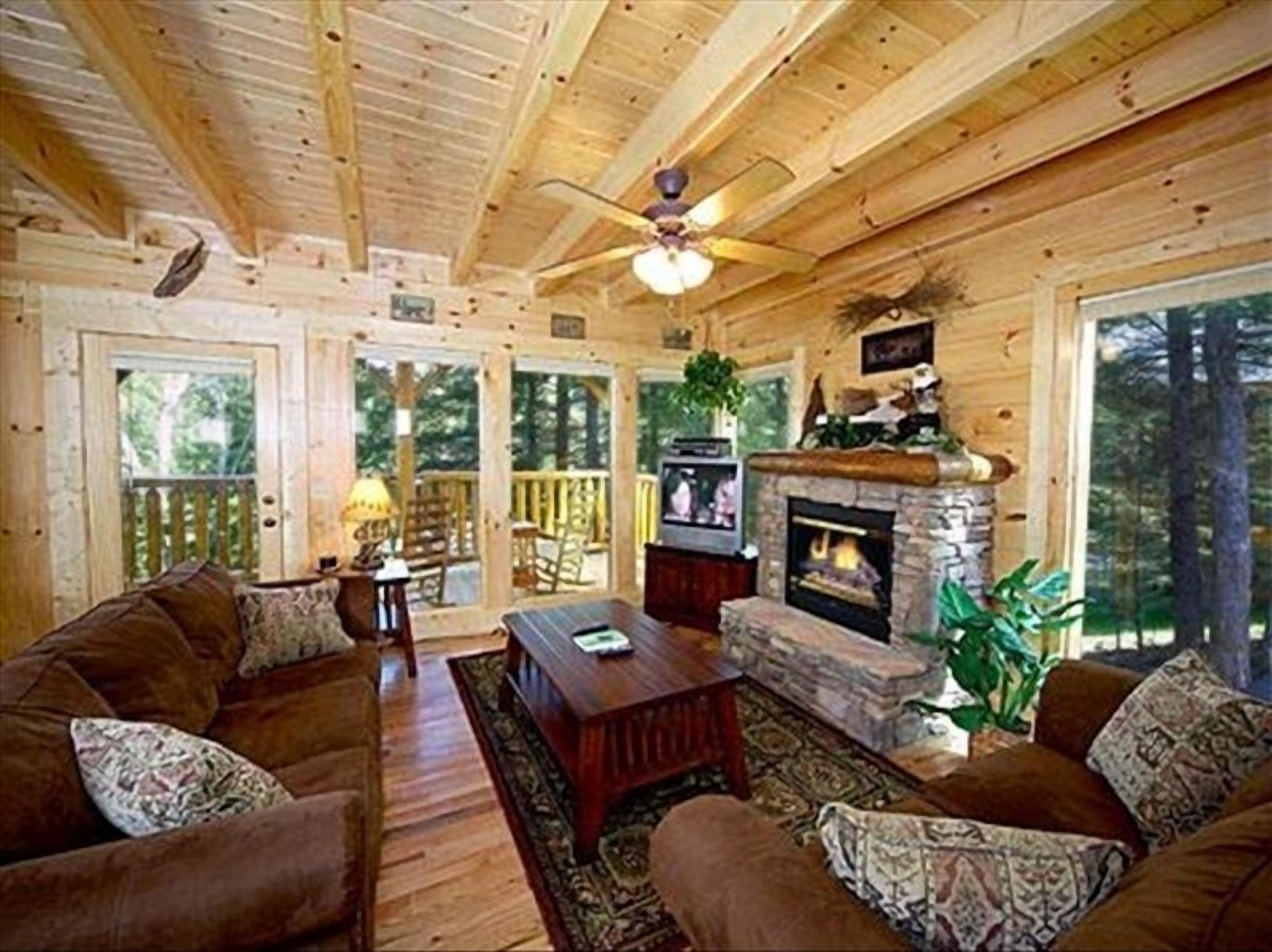 A cozy cabin interior with a fireplace, wooden ceiling, and large windows.