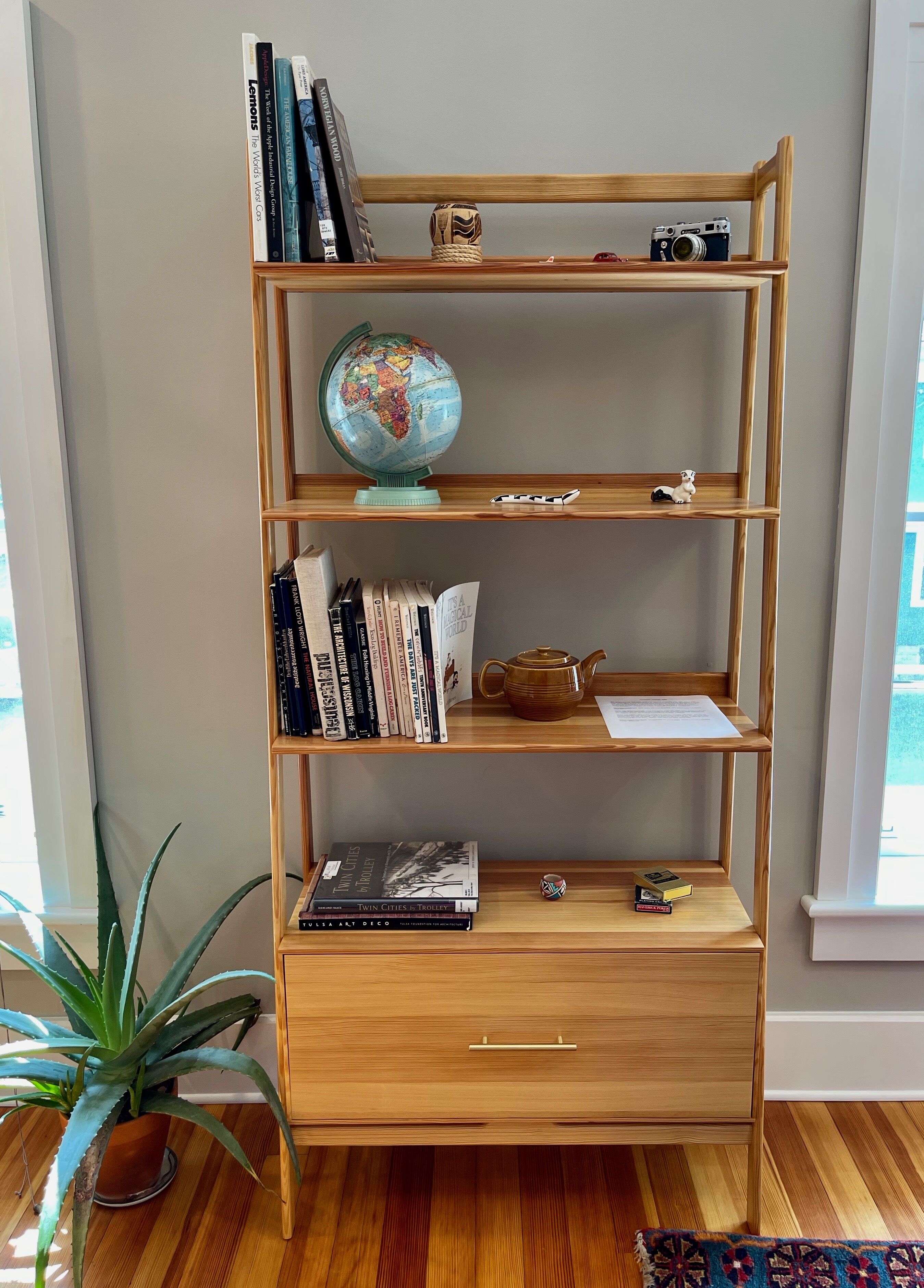 Ein Bücherregal aus Holz mit mehreren Ablagen, ein Globus, eine Kamera und ein Teekessel.