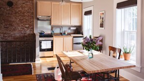 A modern kitchen with wooden cabinets, a brick wall, and a dining area with a wooden table and chairs. - Decorah House- Airy, modern, full of natural light, 5 blocks to downtown (Decorah)