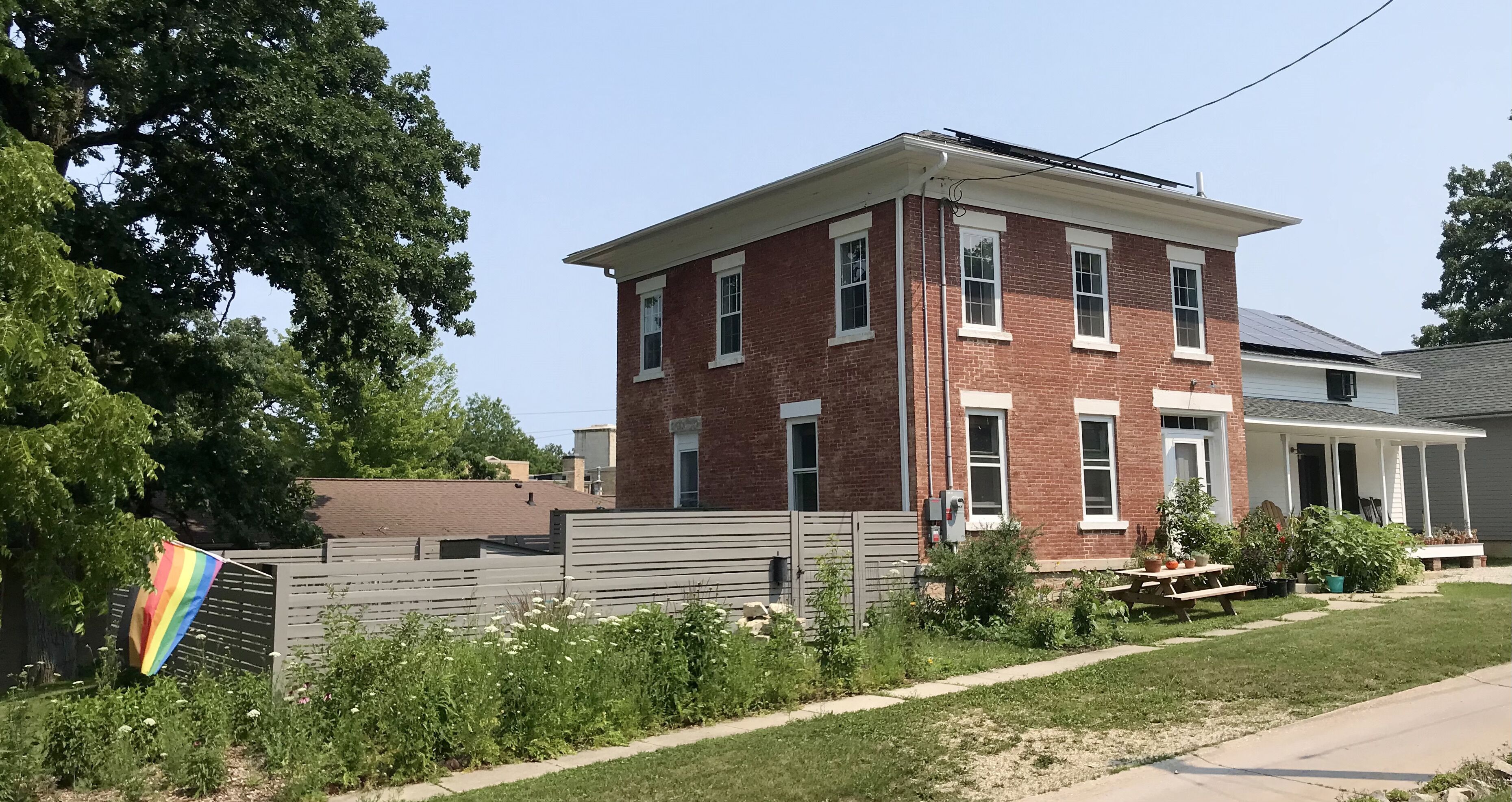 A two-story brick building with a covered porch and a fenced yard.