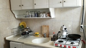 A kitchen with a gas stove, sink, and cabinets. There are various kitchen items on the counter and shelves above. - Oludeniz Hostel (Fethiye)