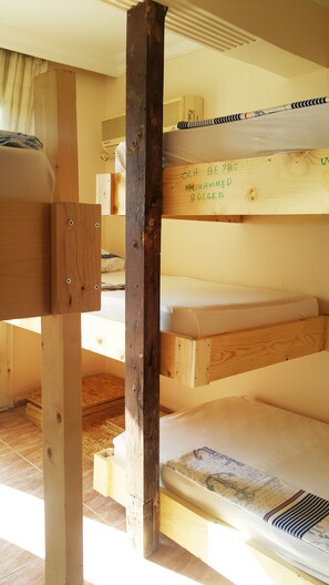 Una cama litera con estructuras de madera y un colchón con almohada a rayas.