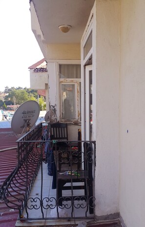 Un balcón con antena parabólica, barandilla metálica y puerta que da a un espacio interior.