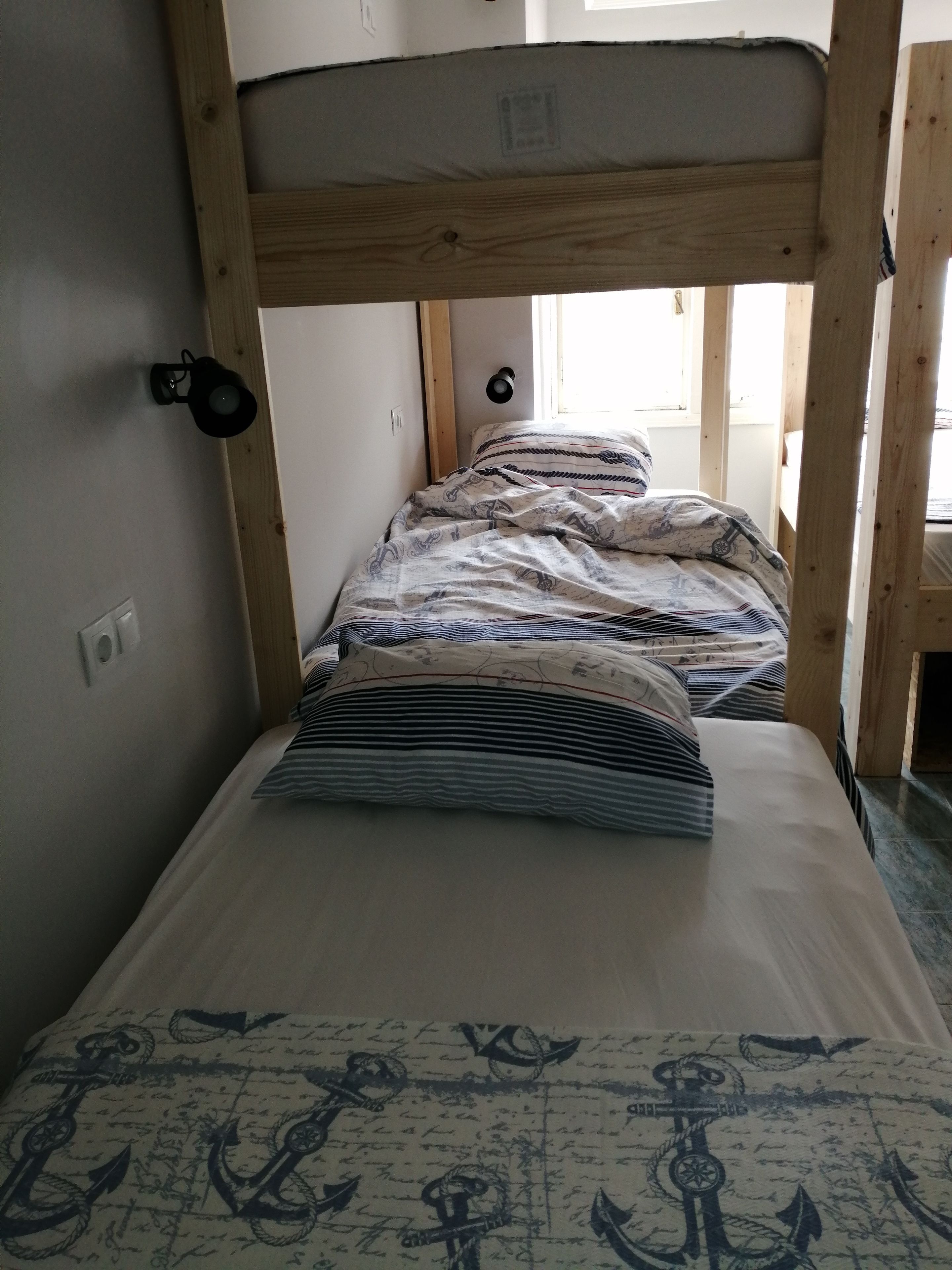 Una cama litera con cabecera de madera, una lámpara negra de pared y ropa de cama estampada.