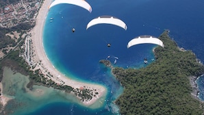 A coastal area with a beach, a forested island, and three paragliders. - Oludeniz Hostel (Fethiye)