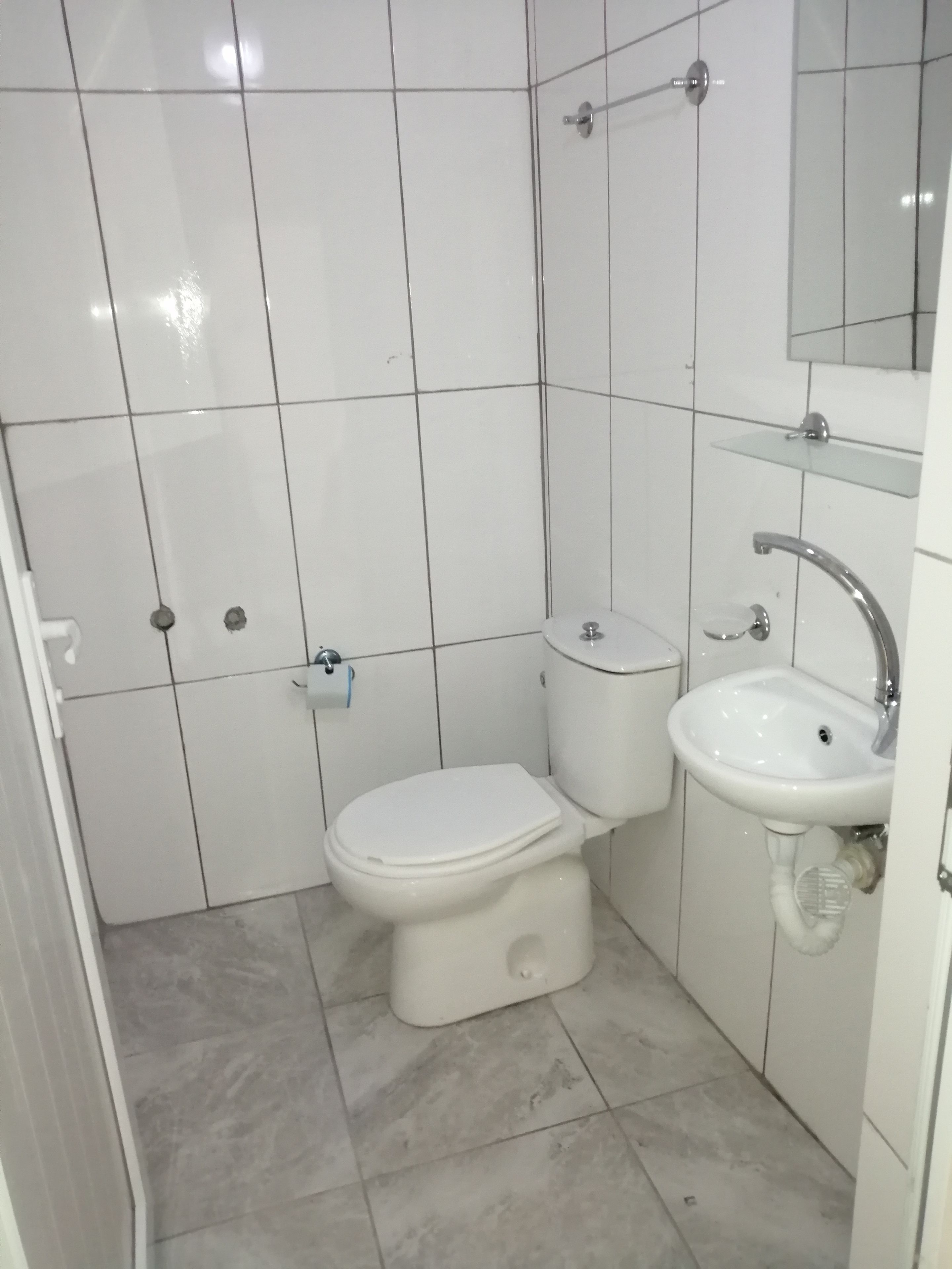 A small, white bathroom with a toilet, sink, and mirror.