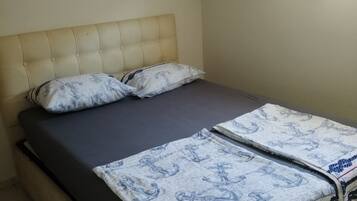 Een eenpersoonsbed met hoofdbord, matras en twee kussens. Er is een airconditioningunit aan de muur bevestigd.