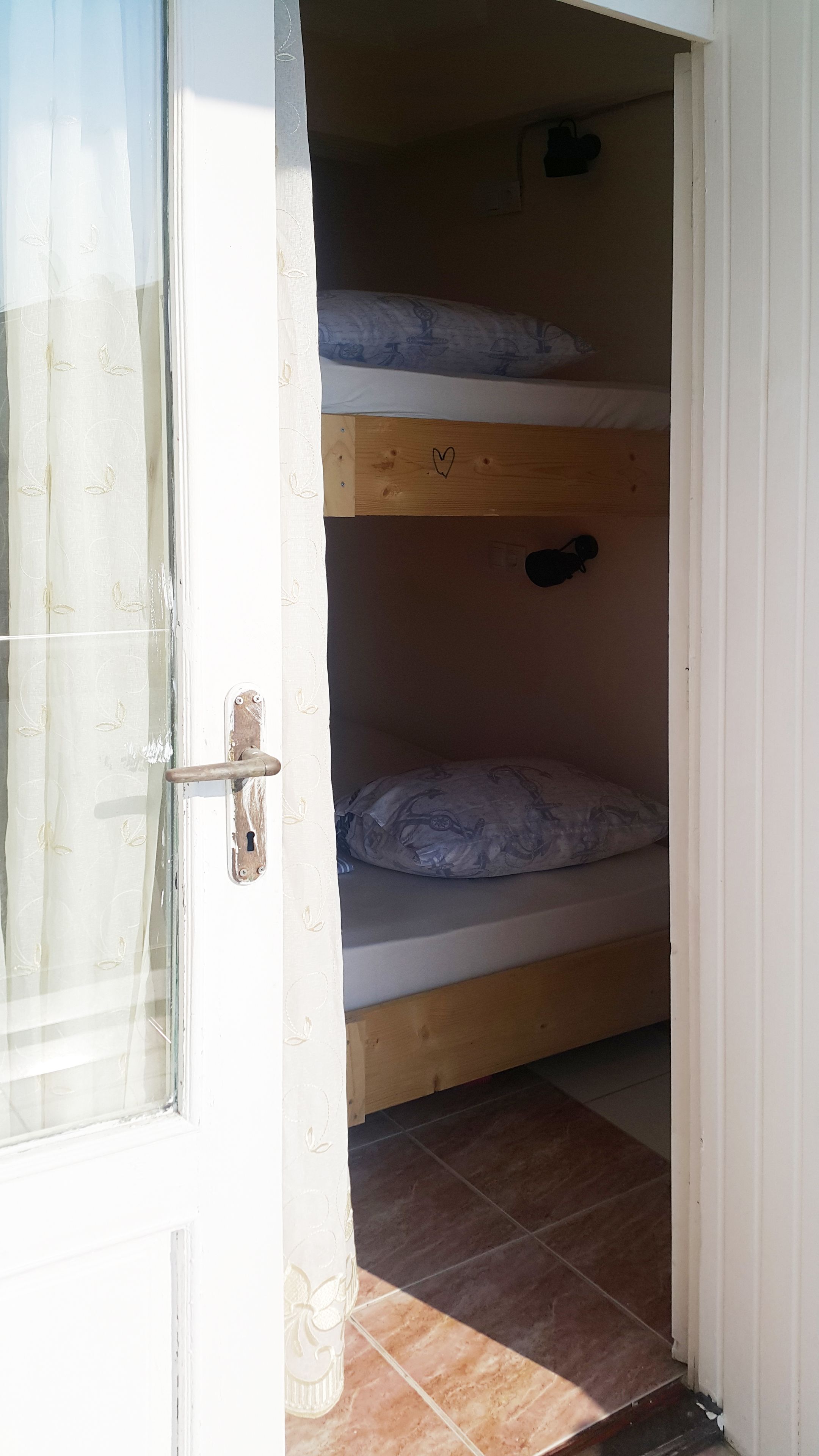 A room with a wooden bunk bed, a door with a handle, and a tiled floor.
