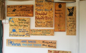 Una pared con varios carteles que indican servicios y comodidades como safari en jeep, buceo, paseos a caballo, desayuno, taquillas y WiFi gratuito.