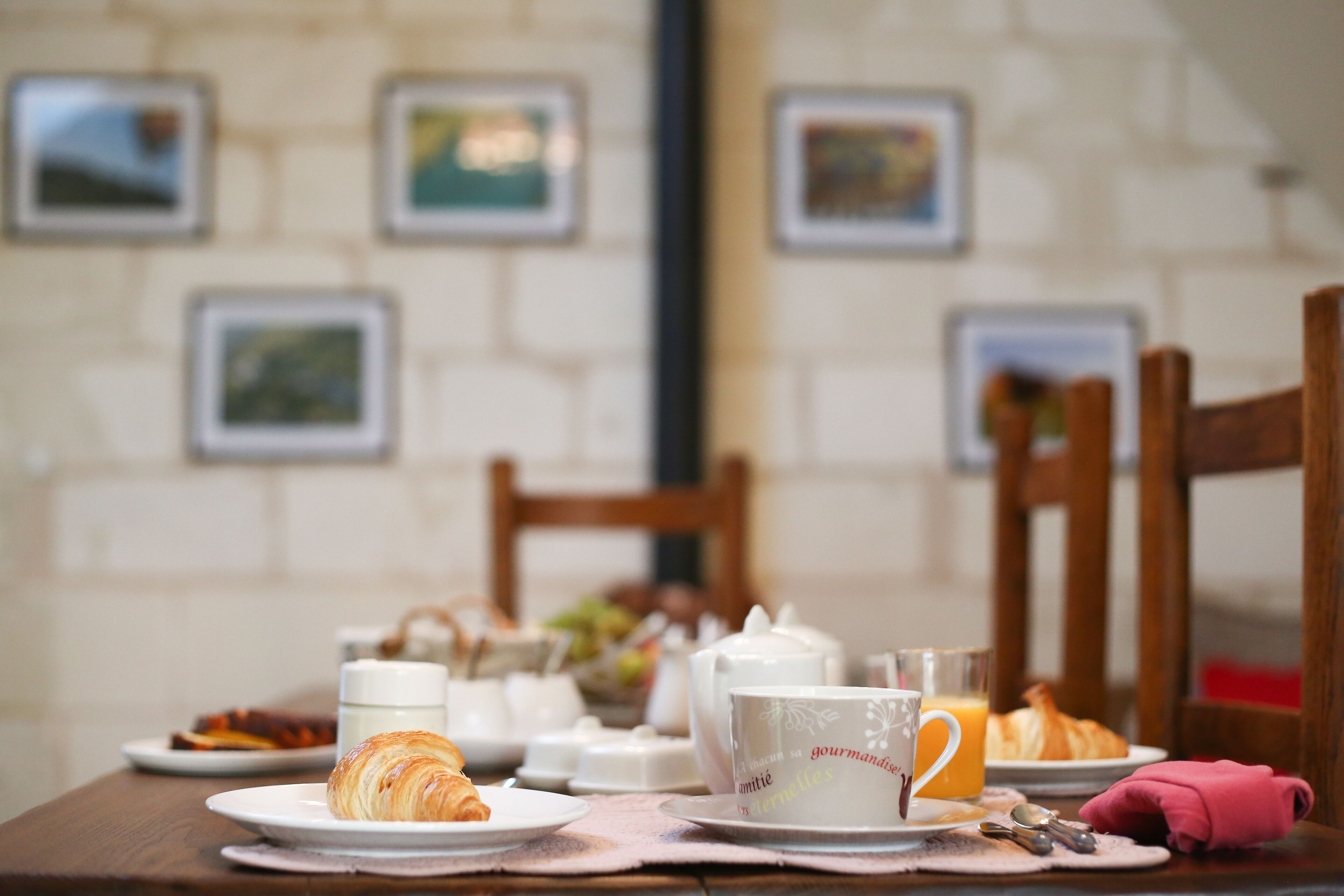 Una mesa de desayuno con cruasanes, una taza de café, un tetera, un vaso de zumo de naranja y un plato de comida.