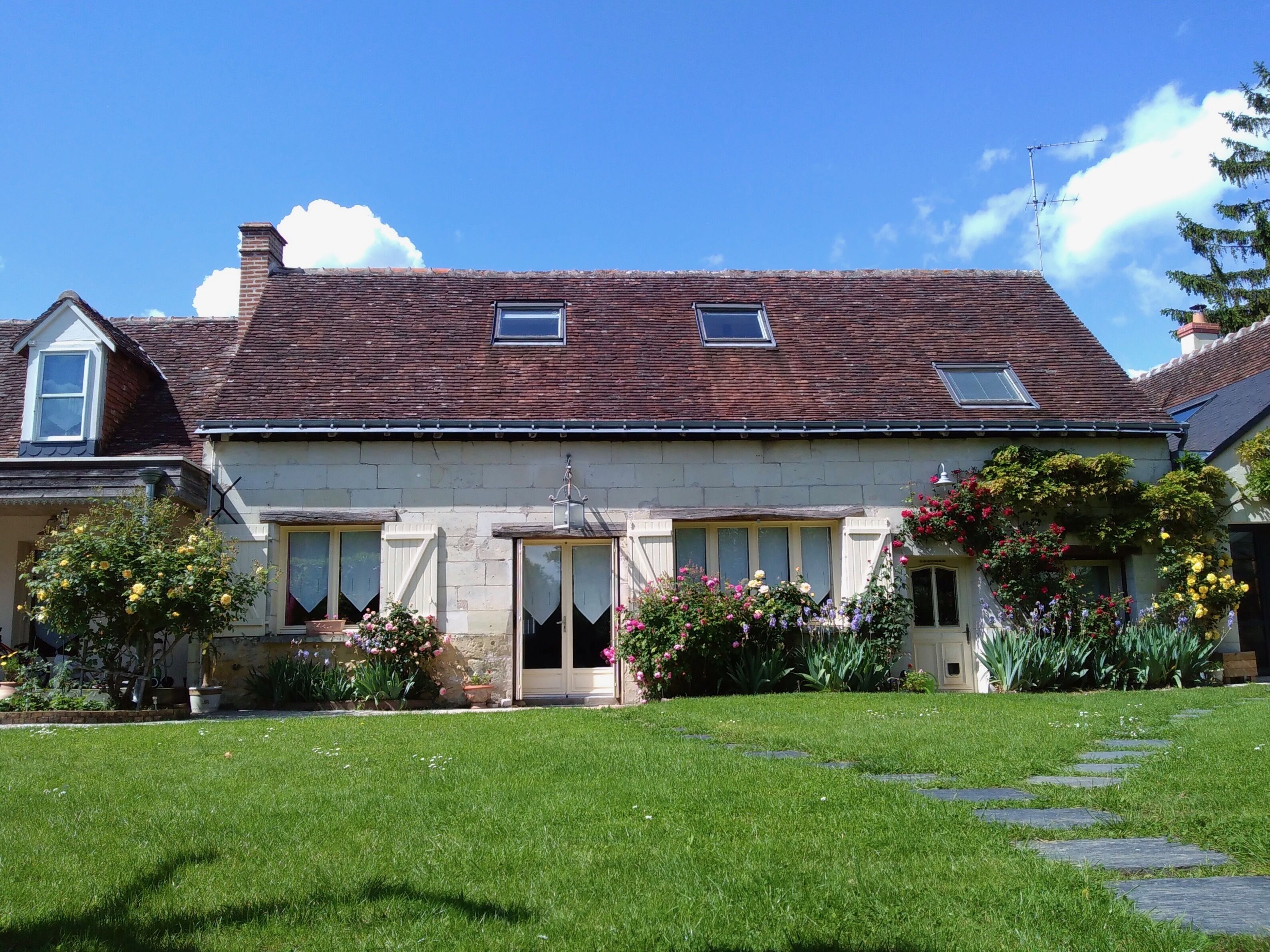 A two-story house with a tiled roof, a front door, and a small porch area with potted plants and flowers.