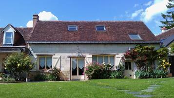 A two-story house with a tiled roof, a front door, and a small porch area with potted plants and flowers.