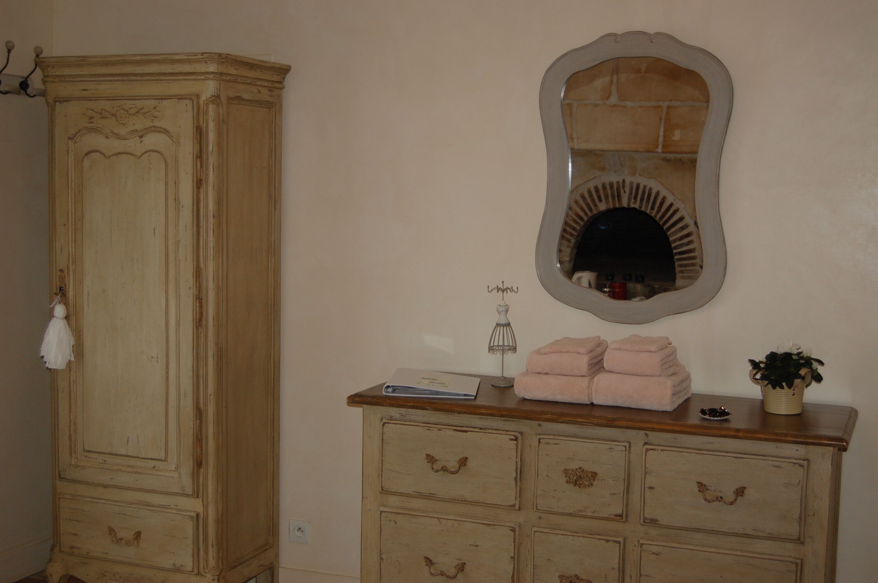 A room with a large armoire, a mirror, a dresser with drawers, and a small plant.