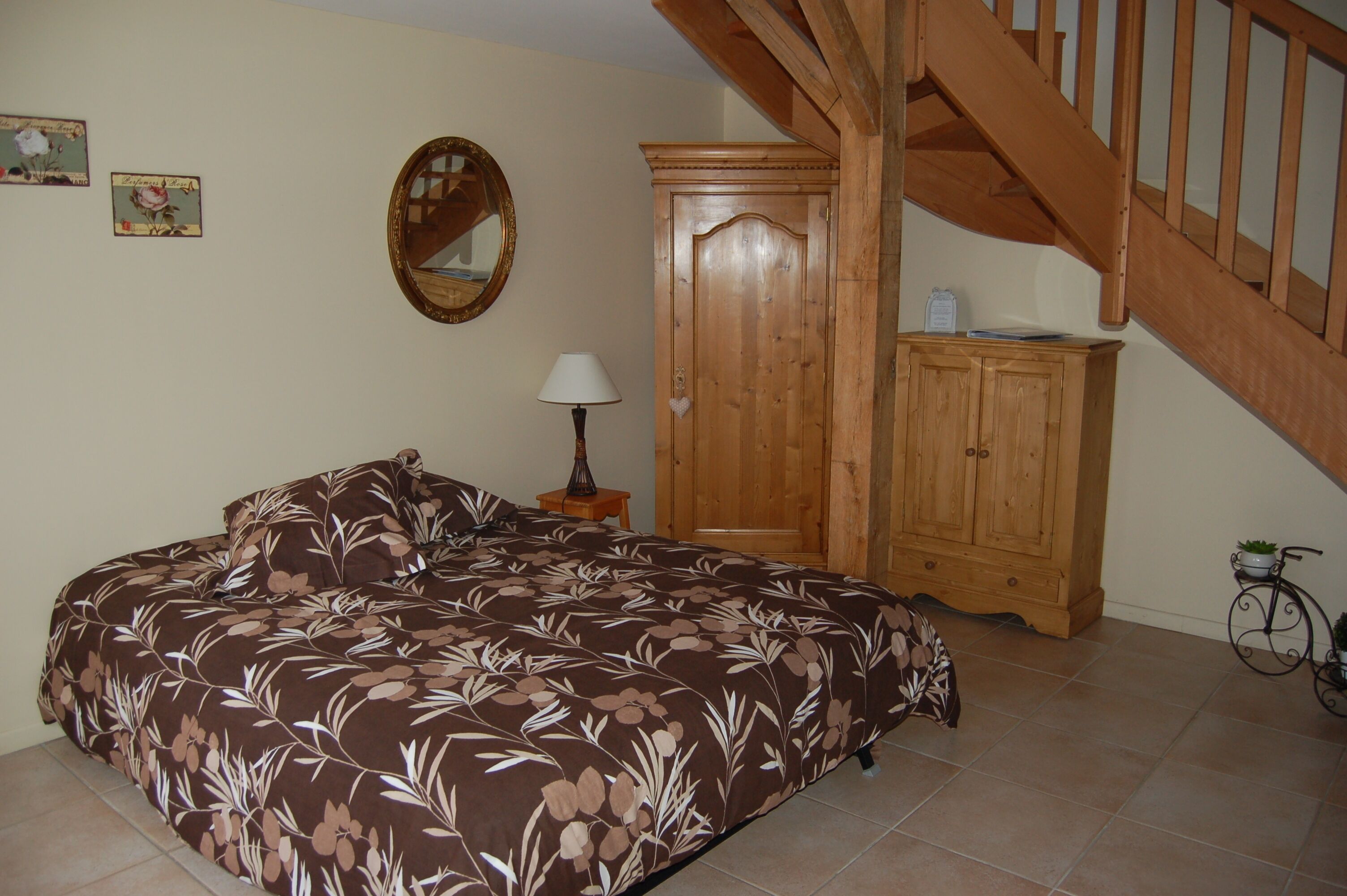 A bedroom with a bed, wooden wardrobe, a mirror, a lamp, and a bicycle.