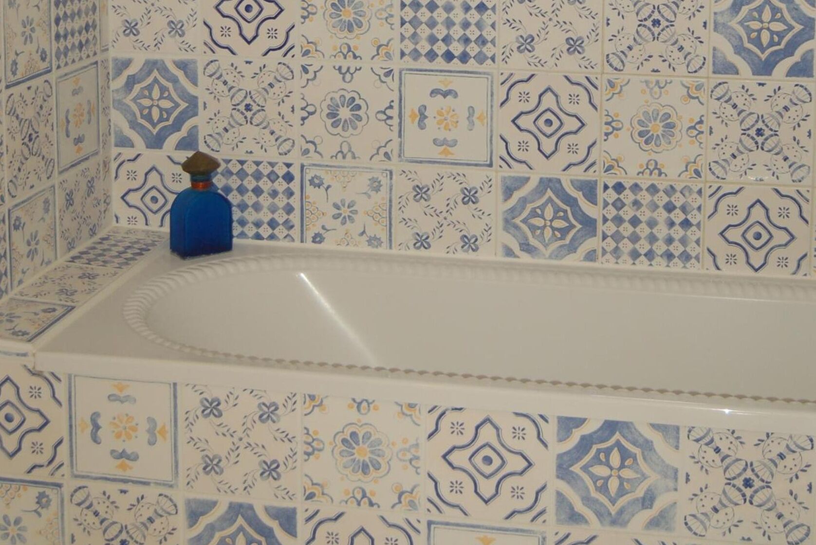 A bathroom with a white bathtub surrounded by patterned tiles.