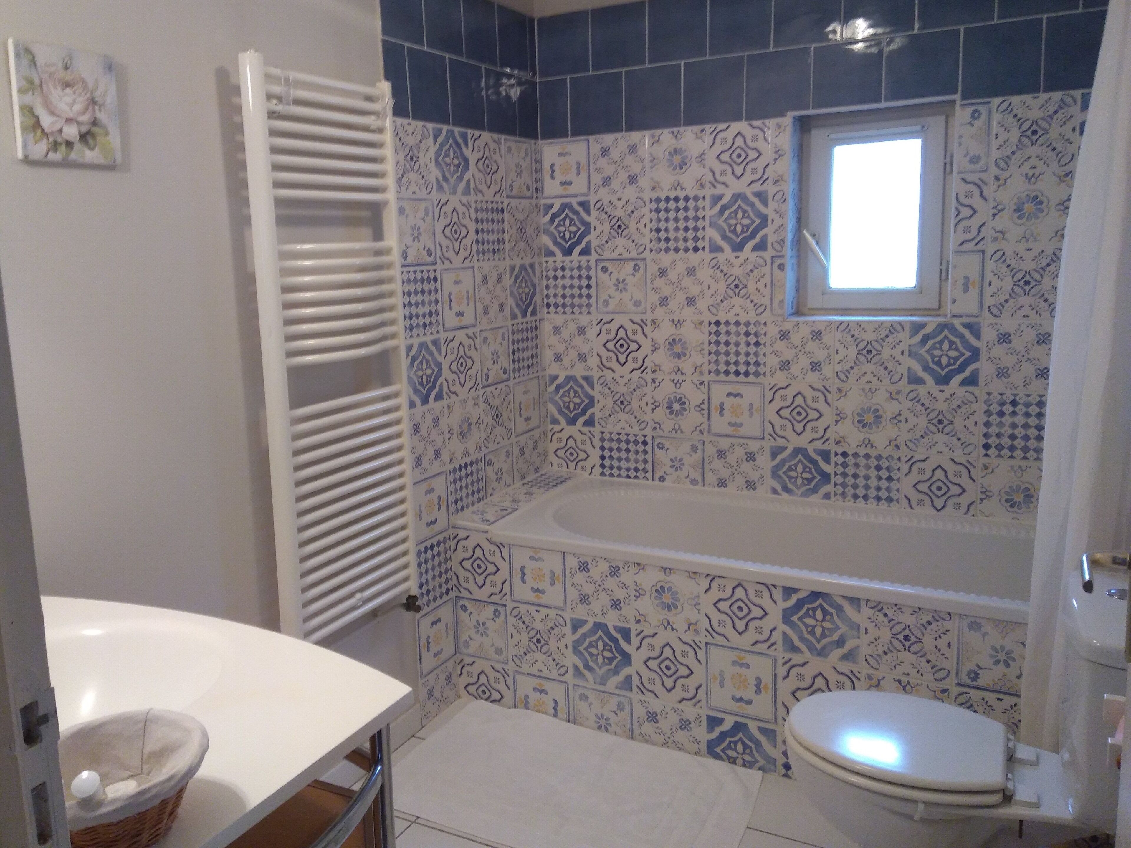 A bathroom with a white bathtub, a white toilet, and a sink. The walls are tiled with blue and white patterns.