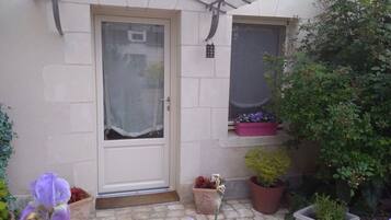 A small house with a front door, a window, and a garden with potted plants and flowers.