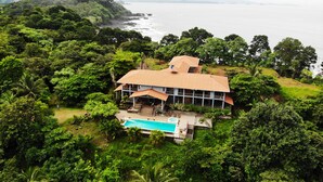 Una casa grande con piscina rodeada de vegetación exuberante y vista al mar.