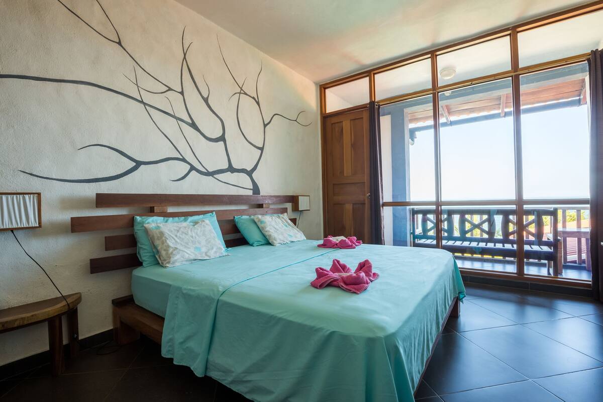 A hotel room with a large bed, a view of the outdoors, and a wall art piece.
