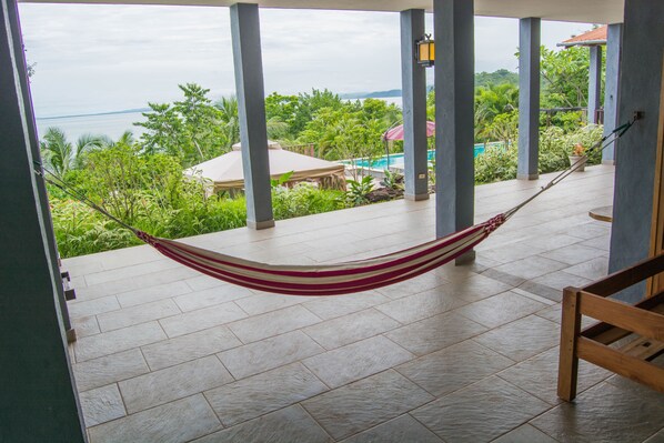 A hammock on a tiled patio with a view of a pool and lush greenery. - Punta Duarte Garden Inn (Torio)
