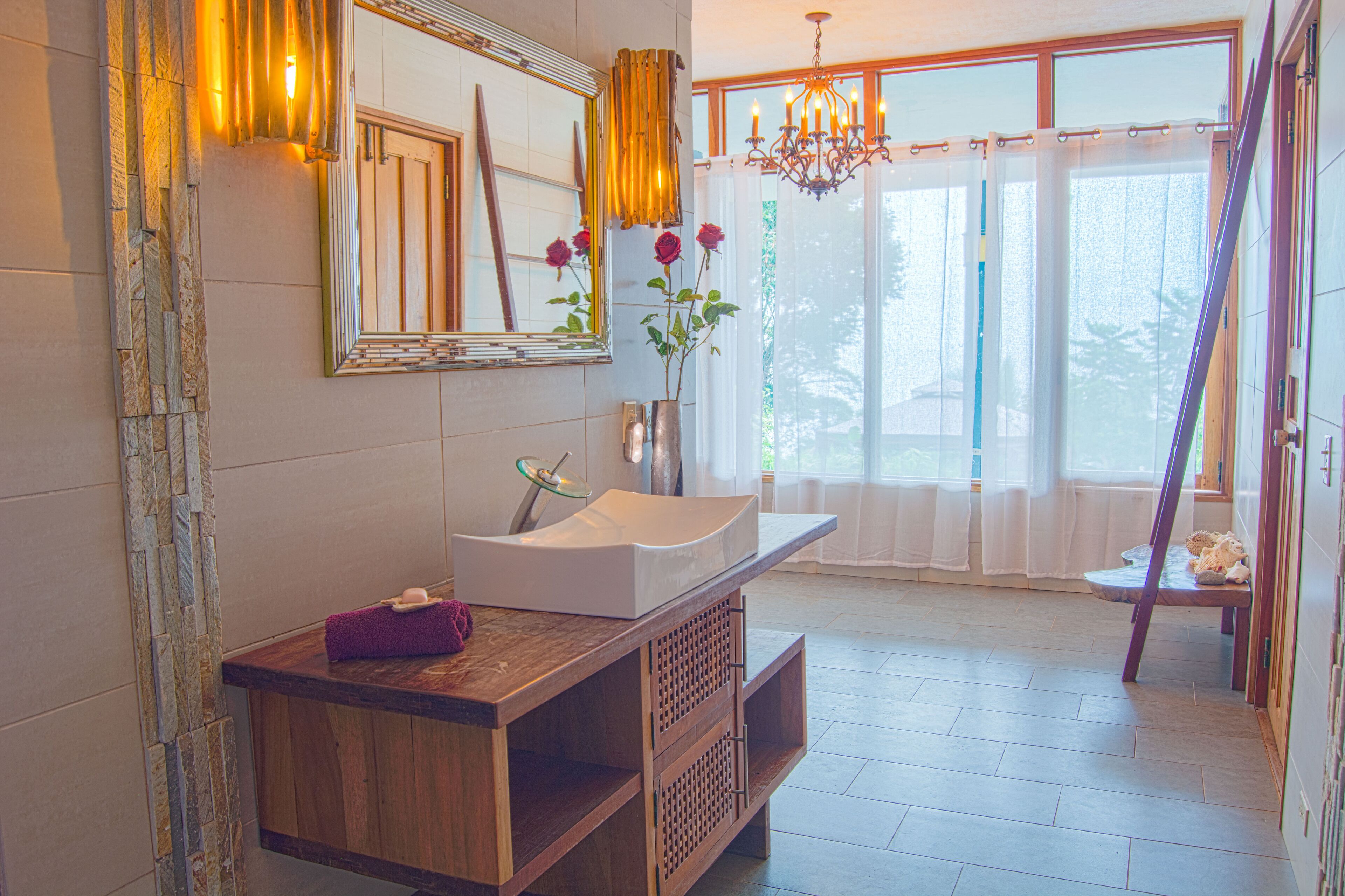 Un baño con tocador de madera, lavamanos blanco, espejo y candelabro.