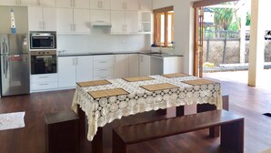 Una cucina moderna con mobili bianchi, forno integrato e microonde. C'è un tavolo da pranzo con tovaglia in pizzo e una panca.