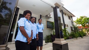 A building with a white facade, large windows, and a covered entrance area with plants. - Renaissance LodgePlus (Port Moresby)