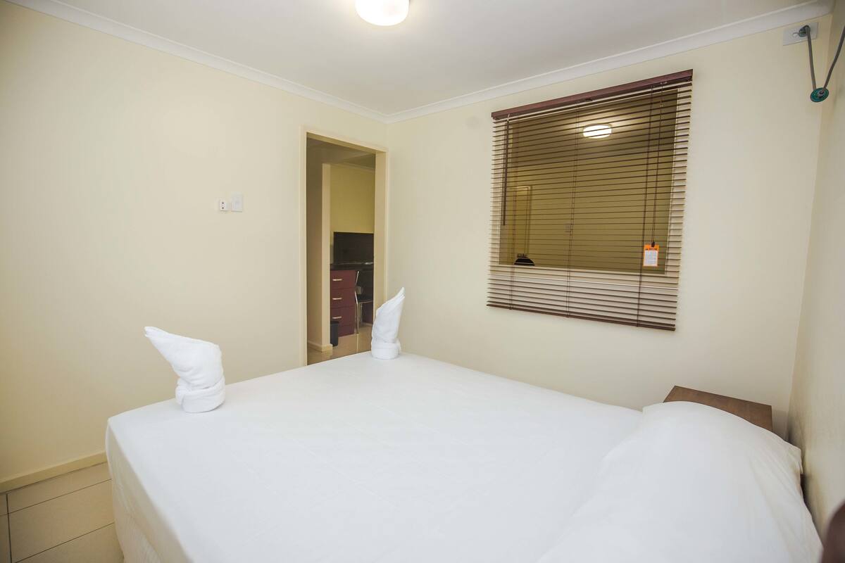 A hotel room with a large bed, a window with blinds, and a door leading to a bathroom.