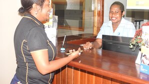 A reception desk with a wooden surface, a glass partition, and a poster on the wall. - Renaissance LodgePlus (Port Moresby)