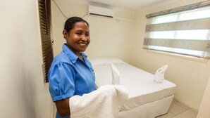 A hotel room with a bed, a window with blinds, and an air conditioning unit on the wall. - Renaissance LodgePlus (Port Moresby)