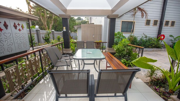 An outdoor patio with a glass table, metal chairs, and a wooden bench. - Renaissance LodgePlus (Port Moresby)