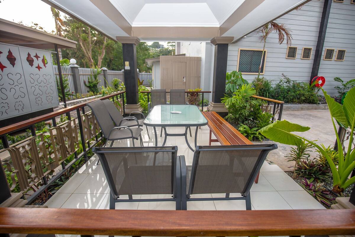 An outdoor patio with a glass table, metal chairs, and a wooden bench.