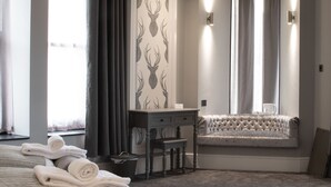 A hotel room with a bed, a desk, a chair, a window with curtains, and a bench by the window. - The Glebe Hotel (Liverpool)