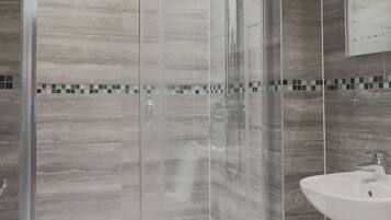 A modern bathroom with a glass-enclosed shower, a white sink, and a tiled floor.