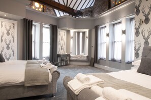 Habitación de hotel con dos camas, zona de estar y ventanas amplias.