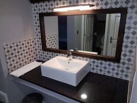 Un bagno con lavandino bianco, piano d'appoggio scuro e uno specchio con cornice in legno.