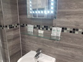Un baño con un estante de vidrio que contiene gel de ducha Eden, un lavabo blanco y un espejo encima.