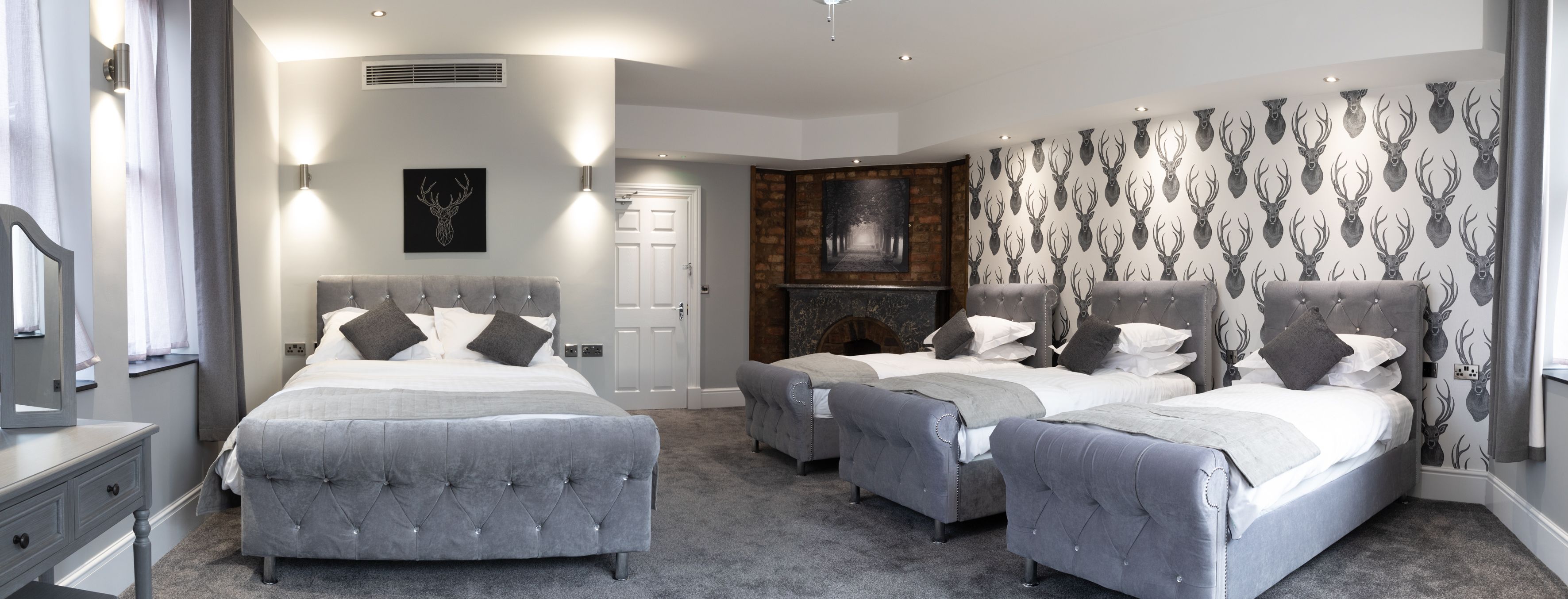A modern bedroom with two large beds, a fireplace, and a patterned wall.