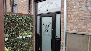 The exterior of The Glibe Hotel with a brick facade, a black door with a deer logo, and a welcome sign. - The Glebe Hotel (Liverpool)
